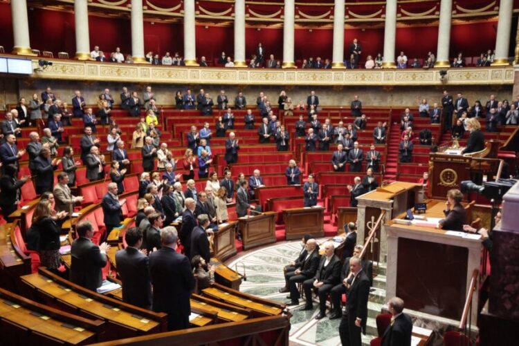 Members of Parliament and members of French government stand in tribute to French journalist Christophe Gleizes before a session of questions to the government at The National Assembly, France's parliament lower house in Paris on February 3, 2026. Gleizes was arrested in May 2024 while travelling to northeastern Algeria's Kabylia region to write about the country's most decorated football club, Jeunesse Sportive de Kabylie. (Photo by Ludovic MARIN / AFP)